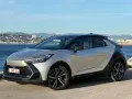 Srebrno-czarna Toyota C-HR na tle morza i miasta. Zastanawiasz się, ile przejedzie hybryda Toyoty na jednym ładowaniu?