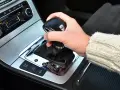 Dłoń trzyma gałkę zmiany biegów w samochodzie. Widoczna jest automatyczna skrzynia biegów DSG z przyciskami ESP, Auto Hold i czujnikami parkowania.