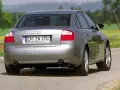 Srebrne Audi B6 sedan z tablicą rejestracyjną IN ZW 370 jedzie po asfaltowej drodze wśród zieleni i żółtych kwiatów.