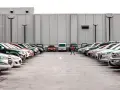 Rząd samochodów na parkingu, jedna osoba idzie pośrodku.