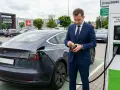 Biznesmen sprawdza portfel przy ładowarce, gdy jego elektryczny samochód pobiera prąd. Na ekranie stacji ładowania widać 38 kW.