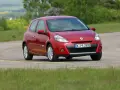 Czerwony Clio 3 na zakręcie drogi, otoczony zielenią.