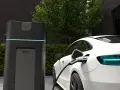 Biała Tesla ładuje się przy nowoczesnej stacji. Wyświetlacz pokazuje "CHARGING 100%", odpowiadając na pytanie, jak długo ładuje się Tesla.