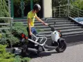 Chłopak w kasku i żółtej koszulce przy białym skuterze. Zastanawiasz się, ile kosztuje karta motorowerowa?
