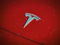 Błyszczące logo Tesli na czerwonej karoserii z kroplami deszczu. Czy Tesla jest tylko elektryczna?