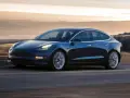 Niebieska Tesla pędzi po drodze, osiągając prędkość do 100 km/h. Tło rozmywa się w złotej poświacie zachodzącego słońca.