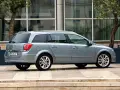 Srebrny Opel Astra H kombi zaparkowany przed nowoczesnym budynkiem z drzewami.