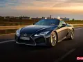 Ciemny Lexus LC 500 z beżowym dachem sunie po drodze podczas zachodu słońca. Sprawdź jego lexus lc 500 cena.
