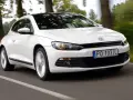 Biały Volkswagen Scirocco pędzi po drodze wśród drzew.
