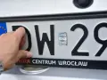 Dłoń dotyka tablicy rejestracyjnej z literami DW i numerem 29. To tablice rejestracyjne województwa dolnośląskiego.