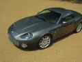 Szary Aston Martin DB9 na żwirowym podjeździe. Zastanawiasz się, ile kosztuje Aston Martin? To auto to marzenie wielu.