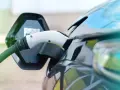 Ładowanie samochodu elektrycznego. Wtyczka podłączona do portu ładowania, zielony kabel biegnie do stacji.
