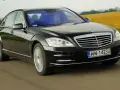 Czarny Mercedes-Benz W221 pędzi po drodze, mijając pola.