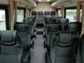 Wnętrze busa z rzędami czarnych, wygodnych siedzeń. Widać, ile miejsc ma bus osobowy, gotowy na podróż.