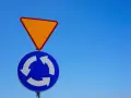 Znak ustąp pierwszeństwa i znak informujący o ruchu okrężnym na tle błękitnego nieba.