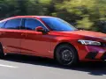 Czerwony Honda Civic 11. generacji pędzi po drodze, otoczony zielenią drzew.