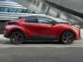 Czerwona Toyota C-HR Hybrid na tle nowoczesnego budynku. Zastanawiasz się, ile kosztuje Toyota C-HR Hybrid?