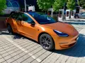 Pomarańczowa Tesla Model 3 na ładowarce. Zastanawiasz się, ile przejedzie Tesla na jednym ładowaniu?