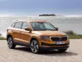 Pomarańczowa Skoda Karoq na tle morza i zamku. Sprawdź aktualny skoda cennik i wybierz swój wymarzony model.