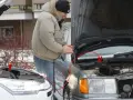 Mężczyzna podłącza kable rozruchowe do samochodu, by odpalić toyotę hybrydę na kable.