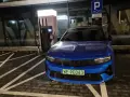 Niebieski samochód elektryczny pod ładowarką. Zastanawiasz się, ile się płaci za ładowanie samochodu elektrycznego?
