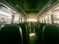 Wnętrze autobusu z rzędami zielonych siedzeń. Trudno ocenić, ile bus ma miejsc, ale wygląda na to, że jest ich sporo.
