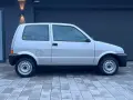Srebrny Fiat Cinquecento na tle ciemnego garażu, z charakterystycznymi felgami i czarnymi zderzakami.