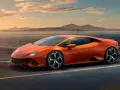Pomarańczowy Lamborghini Huracan pędzi po pustej drodze nad jeziorem o zachodzie słońca.