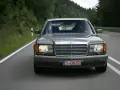 Szary Mercedes W126 jedzie drogą wśród zielonych lasów.