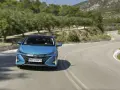 Niebieska Toyota Prius pokonuje zakręt na malowniczej drodze. Zastanawiasz się, ile pali Toyota Prius? Ten model jest znany z oszczędności.