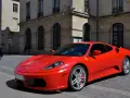 Czerwone Ferrari F430 na brukowanej ulicy przed kamienicą. Zastanawiasz się, ile kosztuje najtańsze Ferrari?