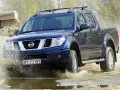 Niebieski Nissan Navara pokonuje wodną przeszkodę, wzbijając fontanny błota.