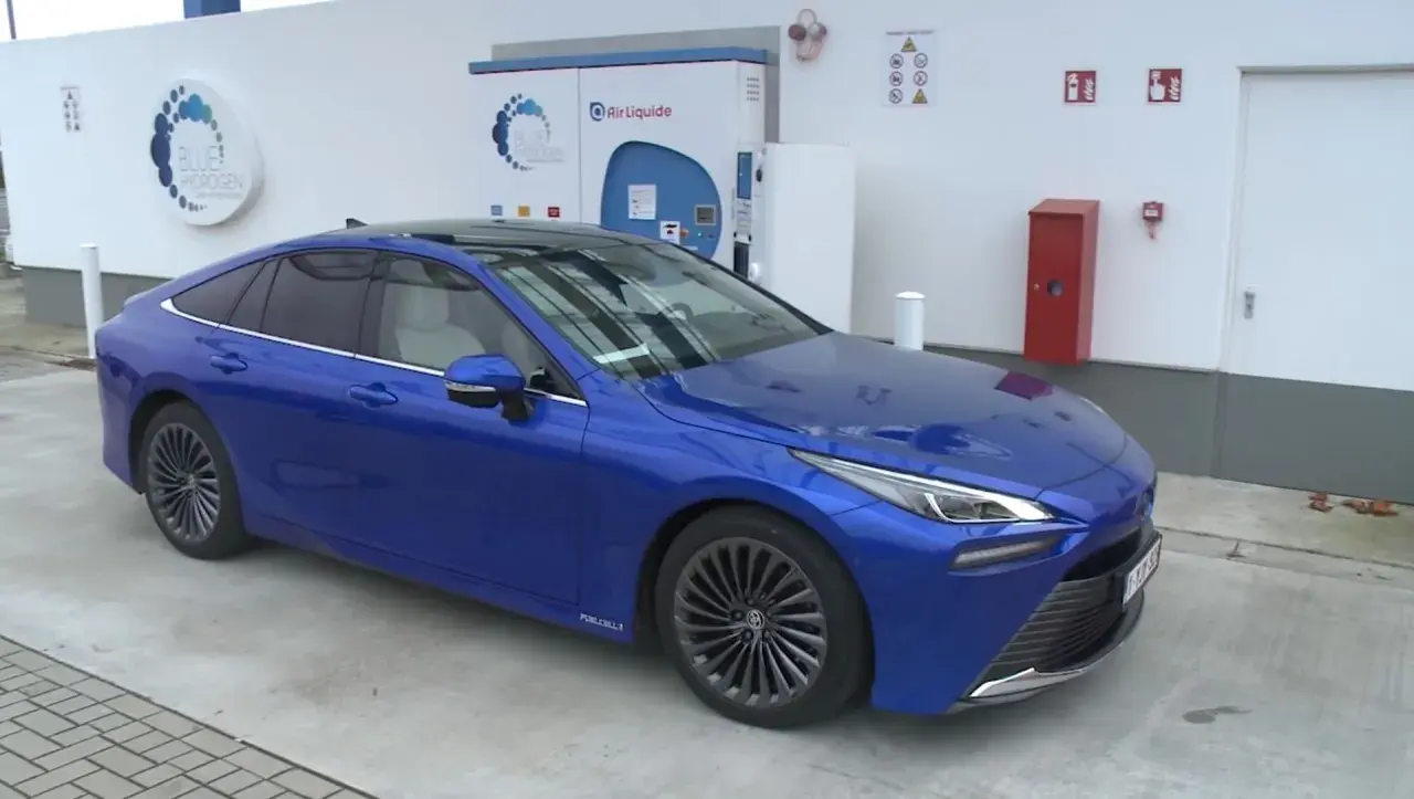 Niebieska Toyota Mirai na stacji wodorowej. Zastanawiasz się nad toyota mirai cena?