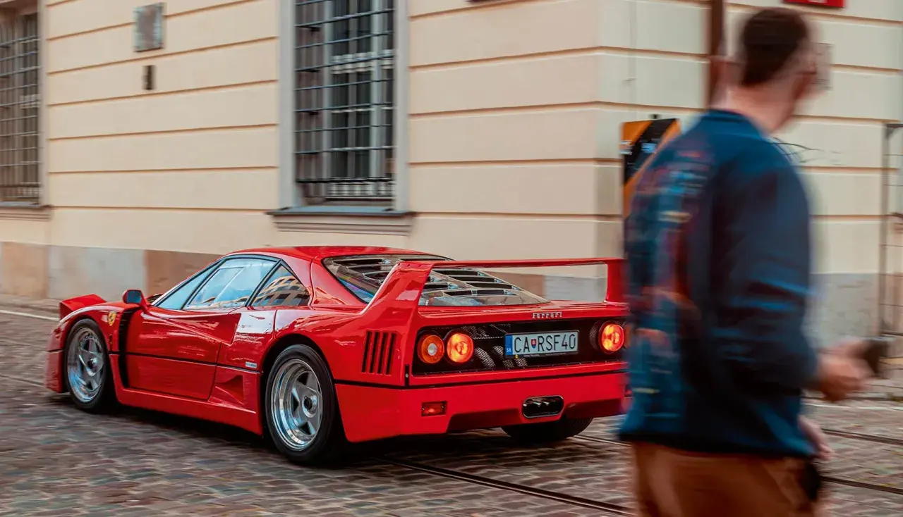 Czerwone Ferrari F40 z tablicą CA RSF40 mija pieszego na brukowanej ulicy.