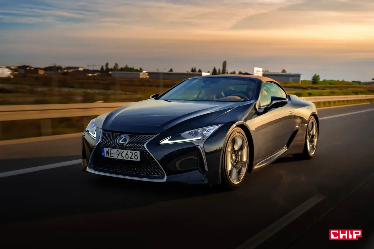 Ciemny Lexus LC 500 z beżowym dachem sunie po drodze podczas zachodu słońca. Sprawdź jego lexus lc 500 cena.