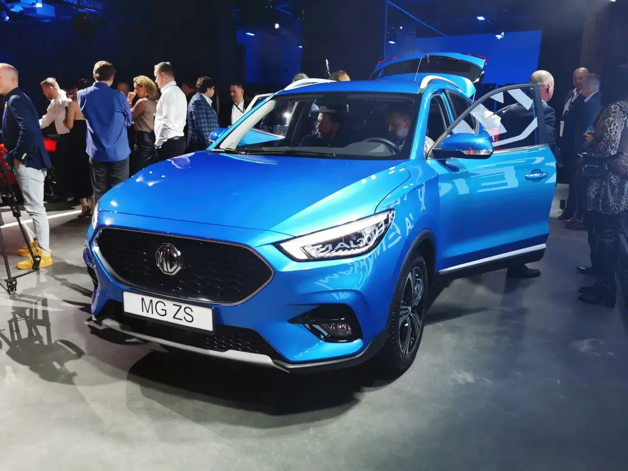 Błękitny MG ZS na prezentacji. Ludzie oglądają nowy model marki MG.