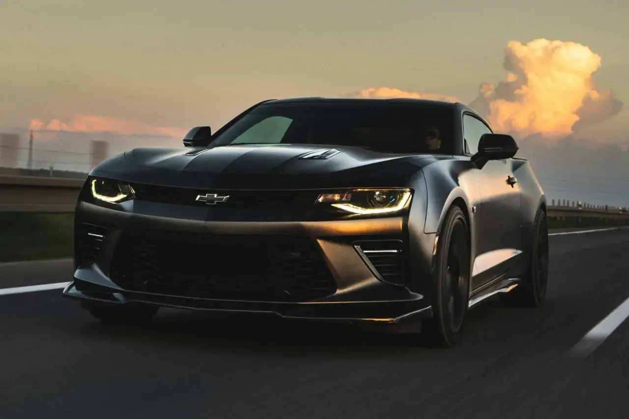 Czarny Chevrolet Camaro pędzi po autostradzie o zachodzie słońca.