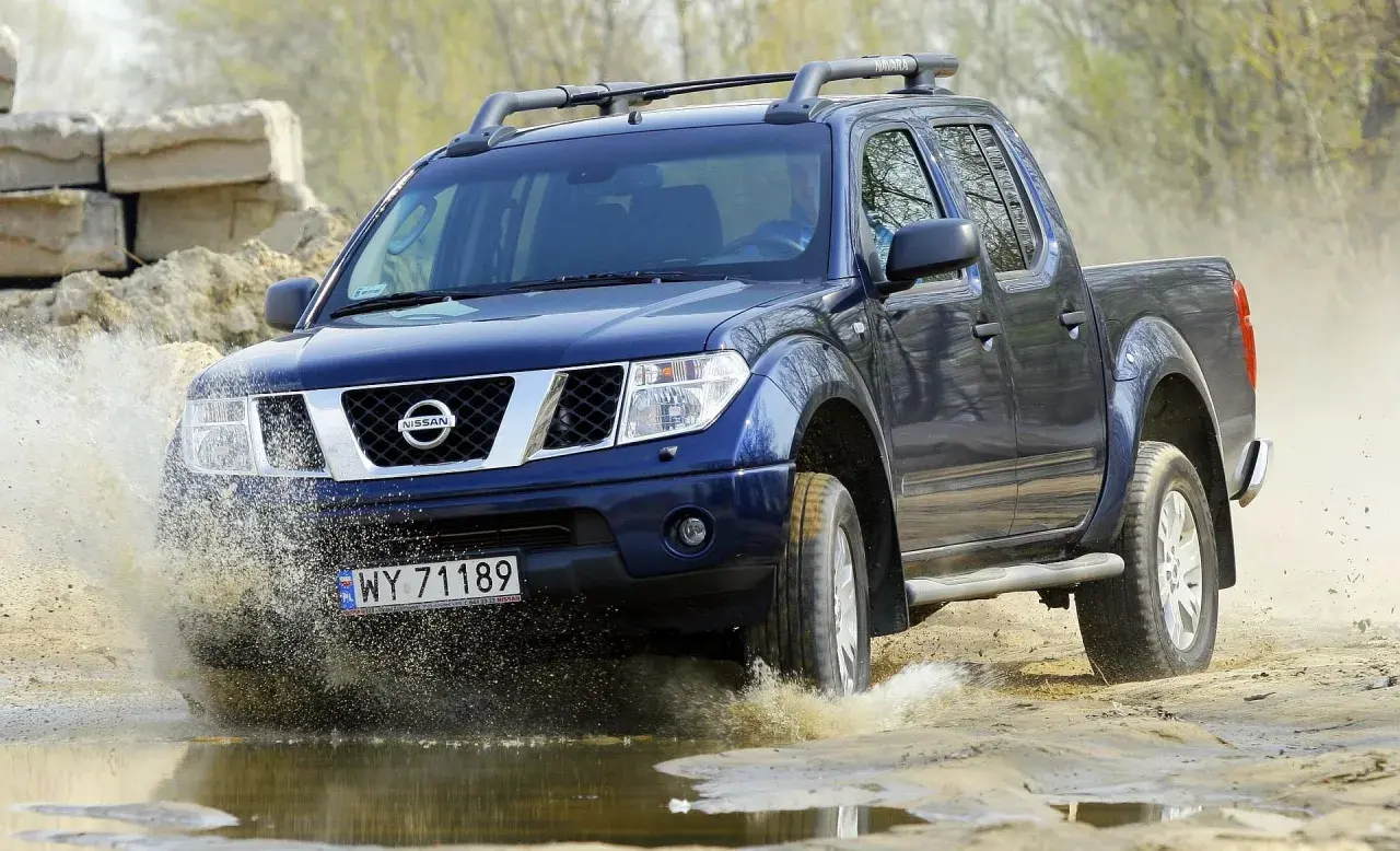 Niebieski Nissan Navara pokonuje wodną przeszkodę, wzbijając fontanny błota.