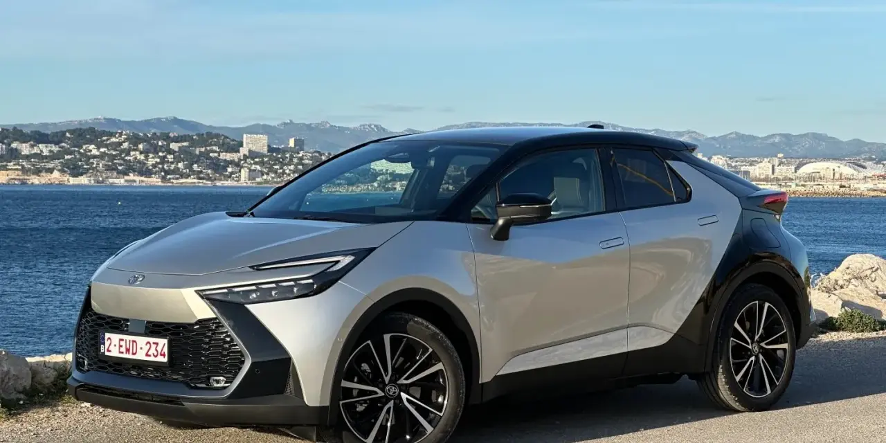 Srebrno-czarna Toyota C-HR na tle morza i miasta. Zastanawiasz się, ile przejedzie hybryda Toyoty na jednym ładowaniu?