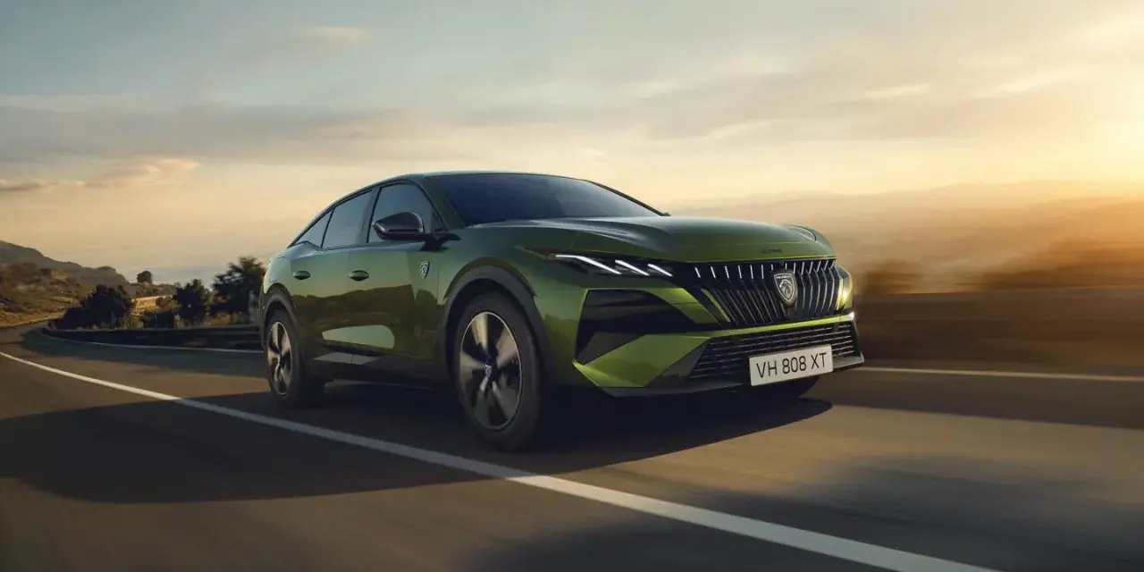 Zielony Peugeot 408 GT sunie po krętej drodze, otoczony malowniczym krajobrazem o zachodzie słońca.