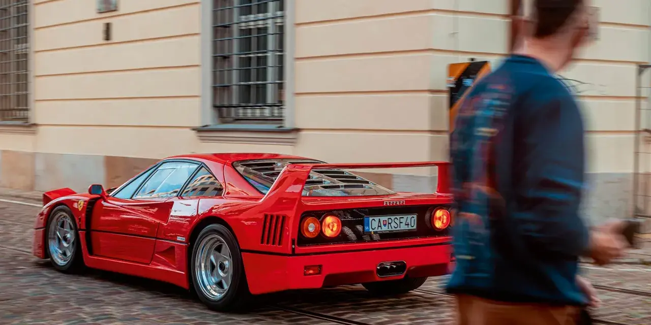 Czerwone Ferrari F40 z tablicą CA RSF40 mija pieszego na brukowanej ulicy.
