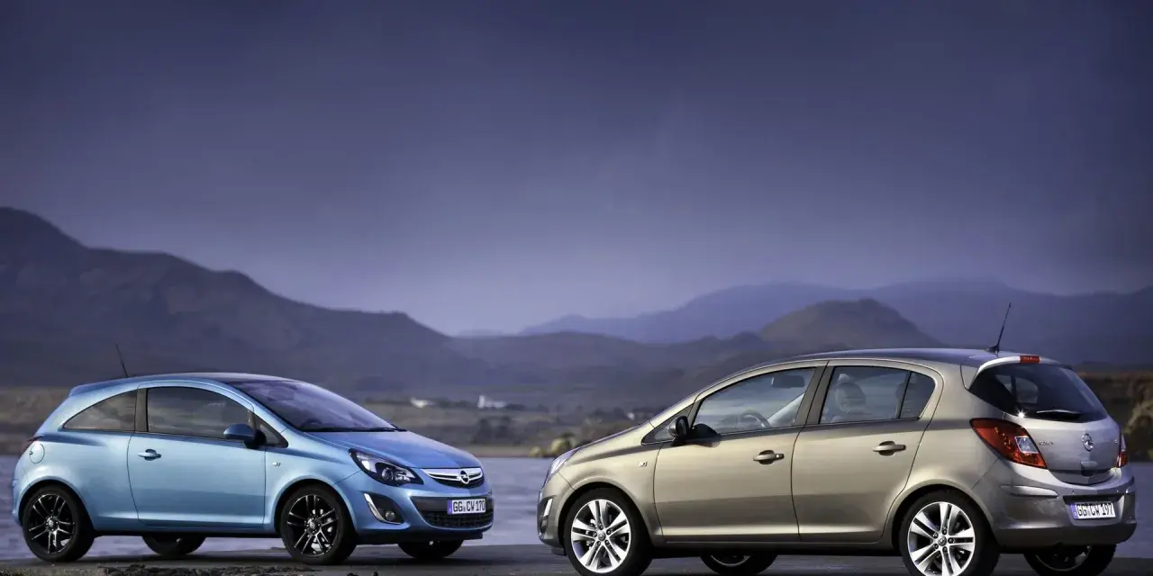 Dwa samochody Opel Corsa D, jeden niebieski, drugi beżowy, stoją na kamiennym murze nad wodą.