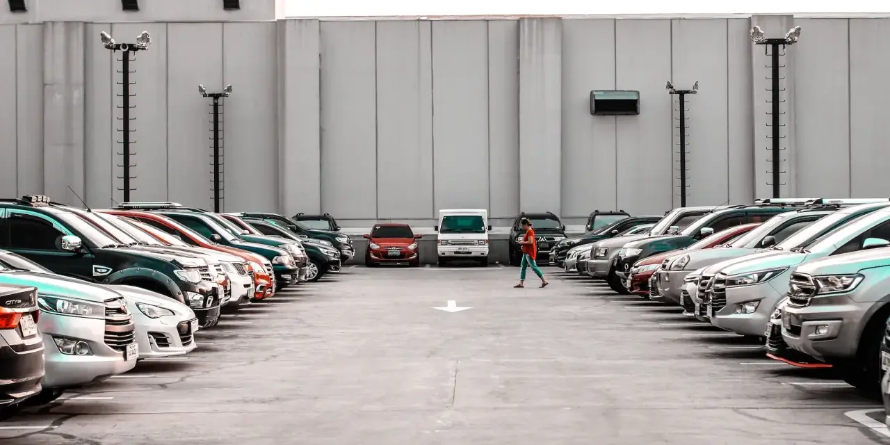Rząd samochodów na parkingu, jedna osoba idzie pośrodku.