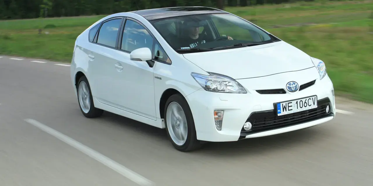 Biała Toyota Prius w ruchu. Czy warto kupić ten hybrydowy samochód?