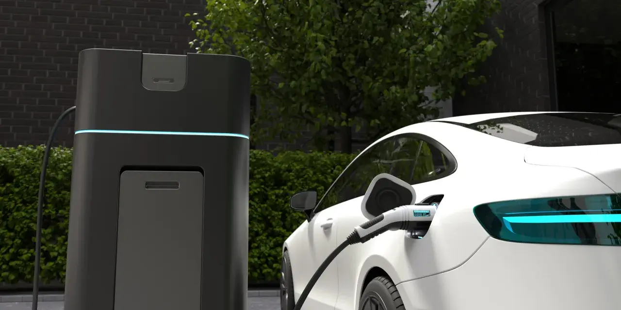 Biała Tesla ładuje się przy nowoczesnej stacji. Wyświetlacz pokazuje "CHARGING 100%", odpowiadając na pytanie, jak długo ładuje się Tesla.