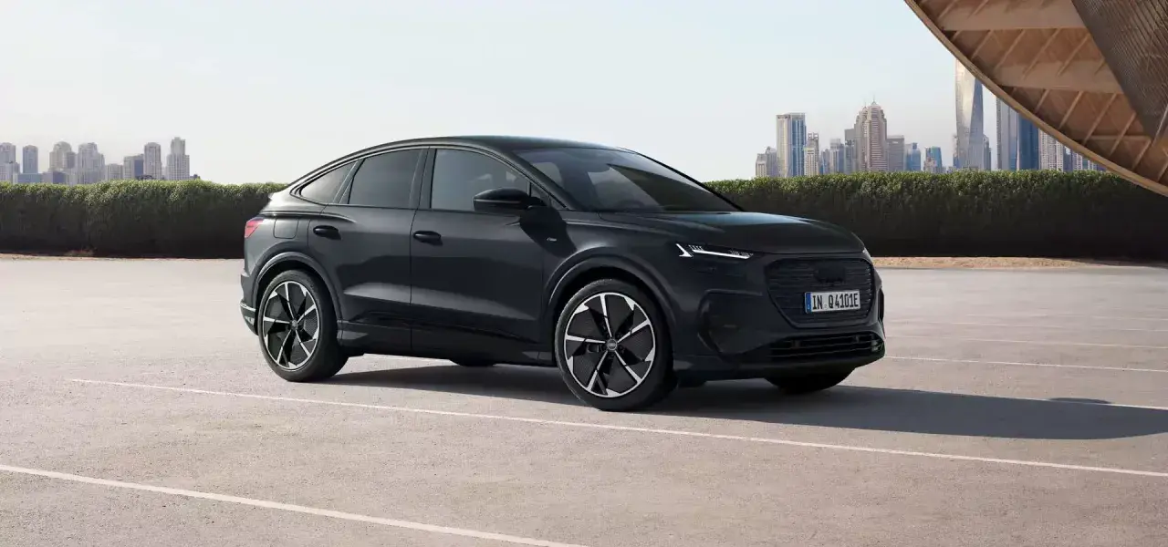 Elegancki, czarny Audi Q4 e-tron, elektryk z dynamiczną linią nadwozia, zaparkowany na tle nowoczesnej panoramy miasta.