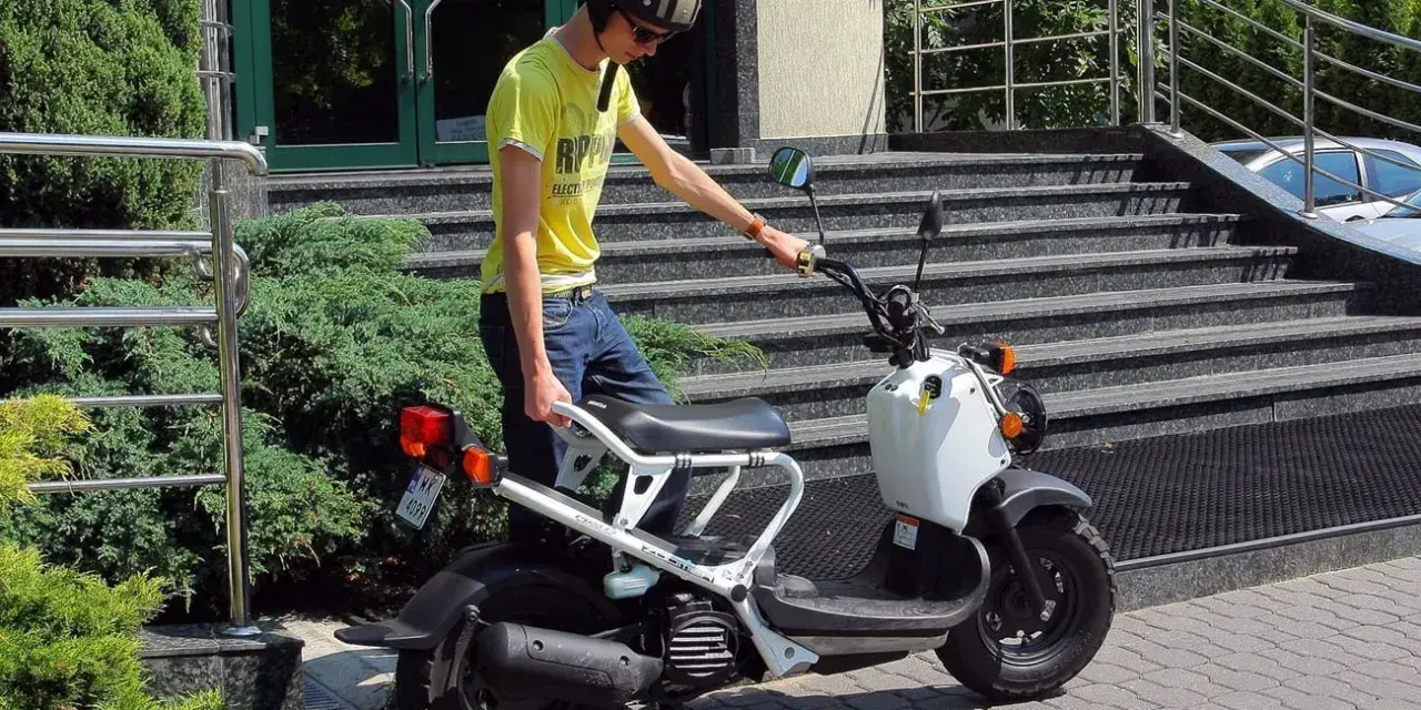 Chłopak w kasku i żółtej koszulce przy białym skuterze. Zastanawiasz się, ile kosztuje karta motorowerowa?