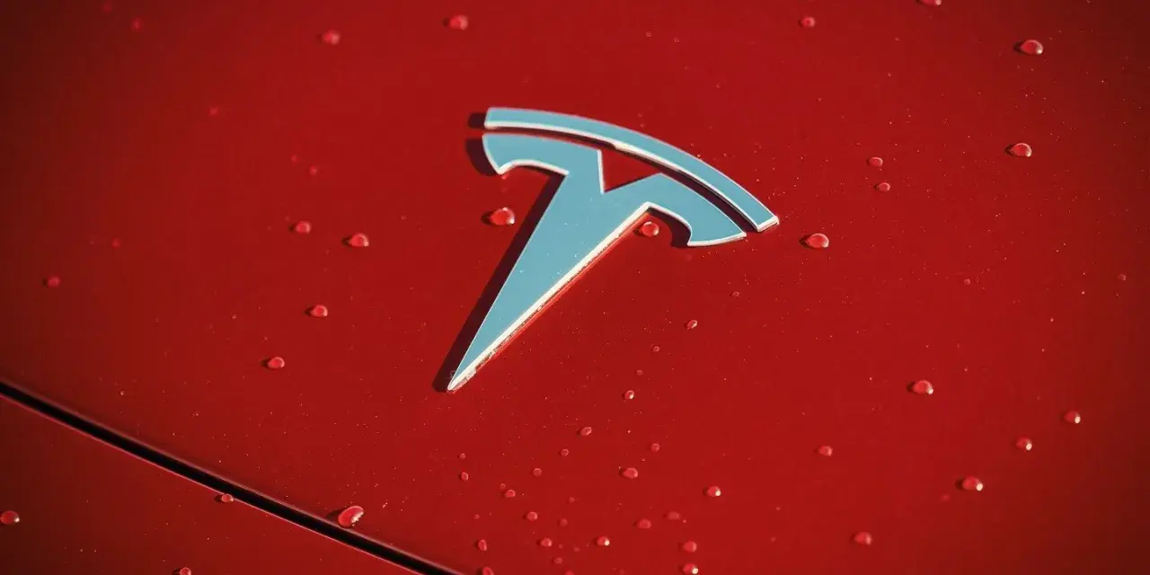 Błyszczące logo Tesli na czerwonej karoserii z kroplami deszczu. Czy Tesla jest tylko elektryczna?