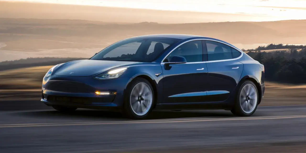 Niebieska Tesla pędzi po drodze, osiągając prędkość do 100 km/h. Tło rozmywa się w złotej poświacie zachodzącego słońca.