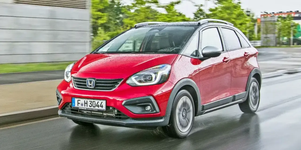 Czerwony Honda Jazz 4 w wersji Crosstar z czarnym dachem i relingami, porusza się po mokrej drodze.